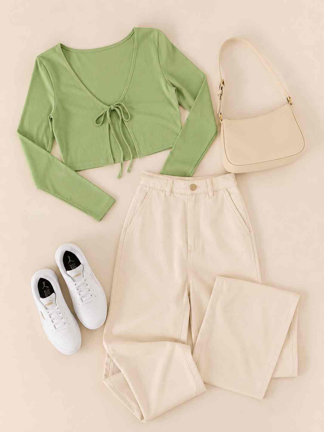 Flat lay fashion photography featuring a sage green tie-front crop top, cream wide-leg trousers, white sneakers, and a beige shoulder bag neatly arranged on a warm beige background in a minimalist Pinterest-inspired aesthetic.