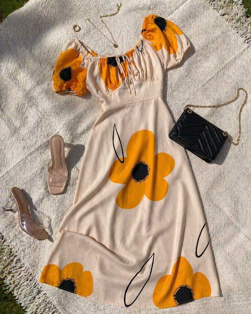 Floral midi dress with yellow flowers styled with clear heels and a black handbag placed on a light blanket in a flat lay summer outfit setup